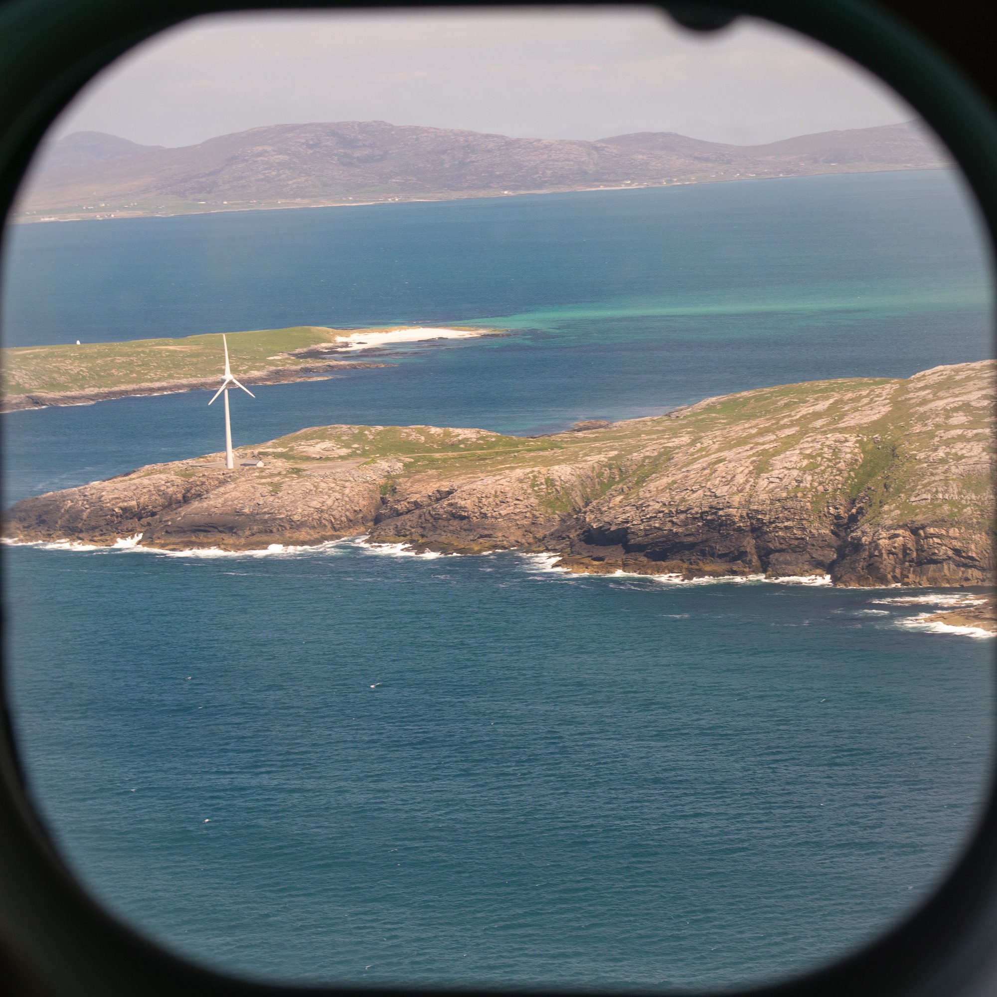 photo of a wind turbine on the coast through a plane window